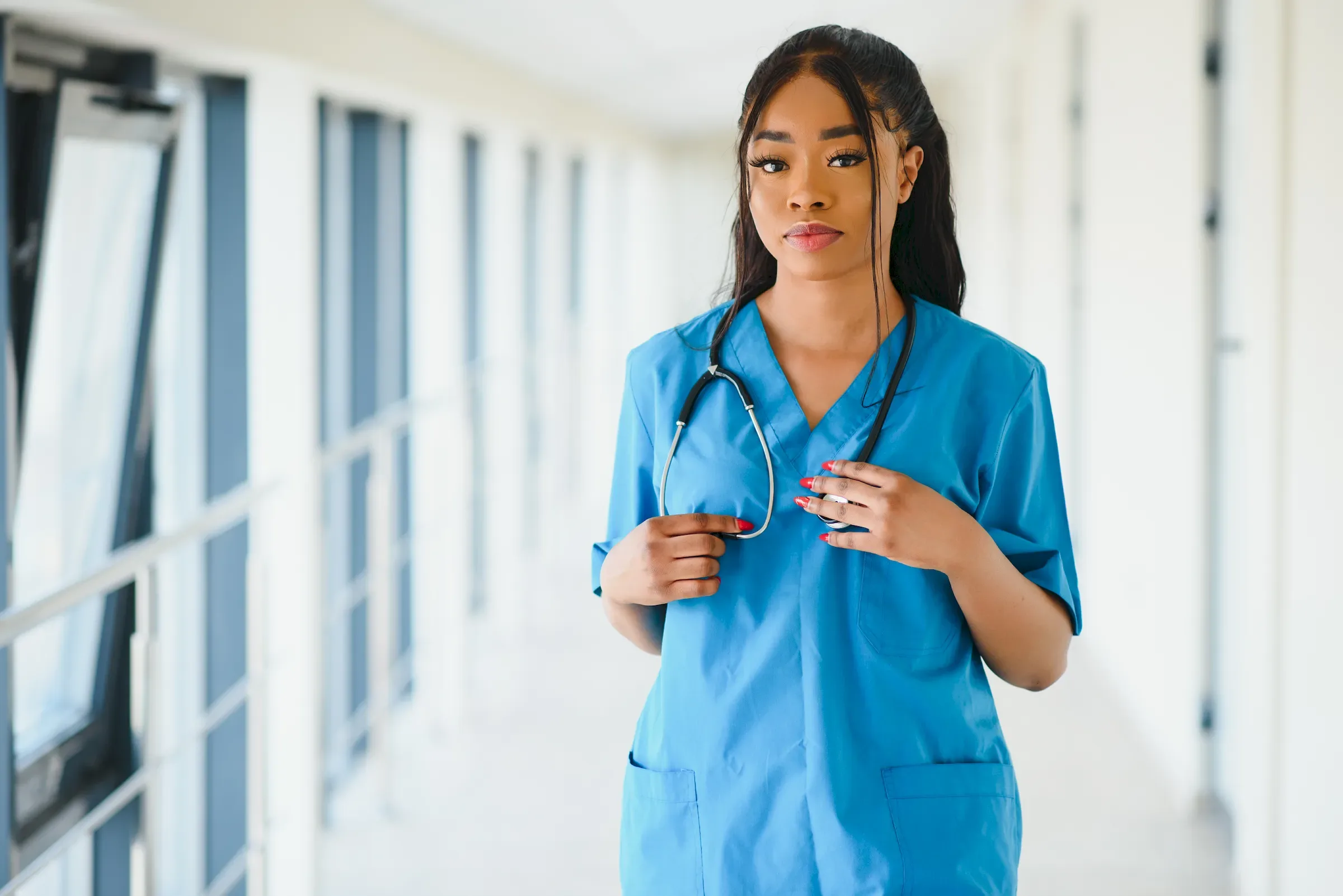 A nurse in scrubs walking along a bright hospital corridor.